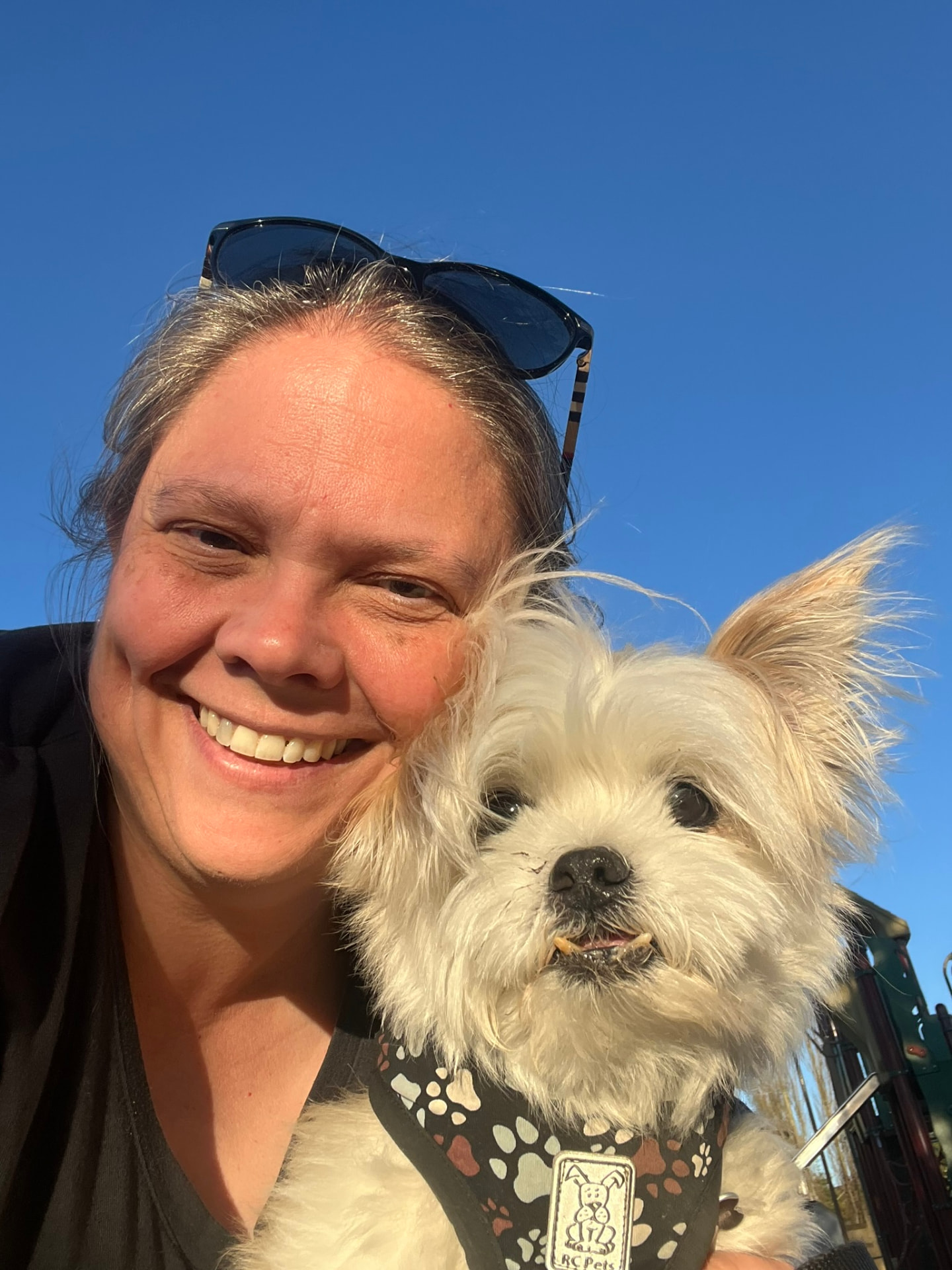 Joy smiling in the sunshine with a happy little white dog